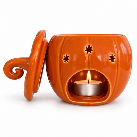 Quemador calabaza naranja con tapa retirada y vela de té encendida visible en la abertura posterior, sobre fondo blanco.
